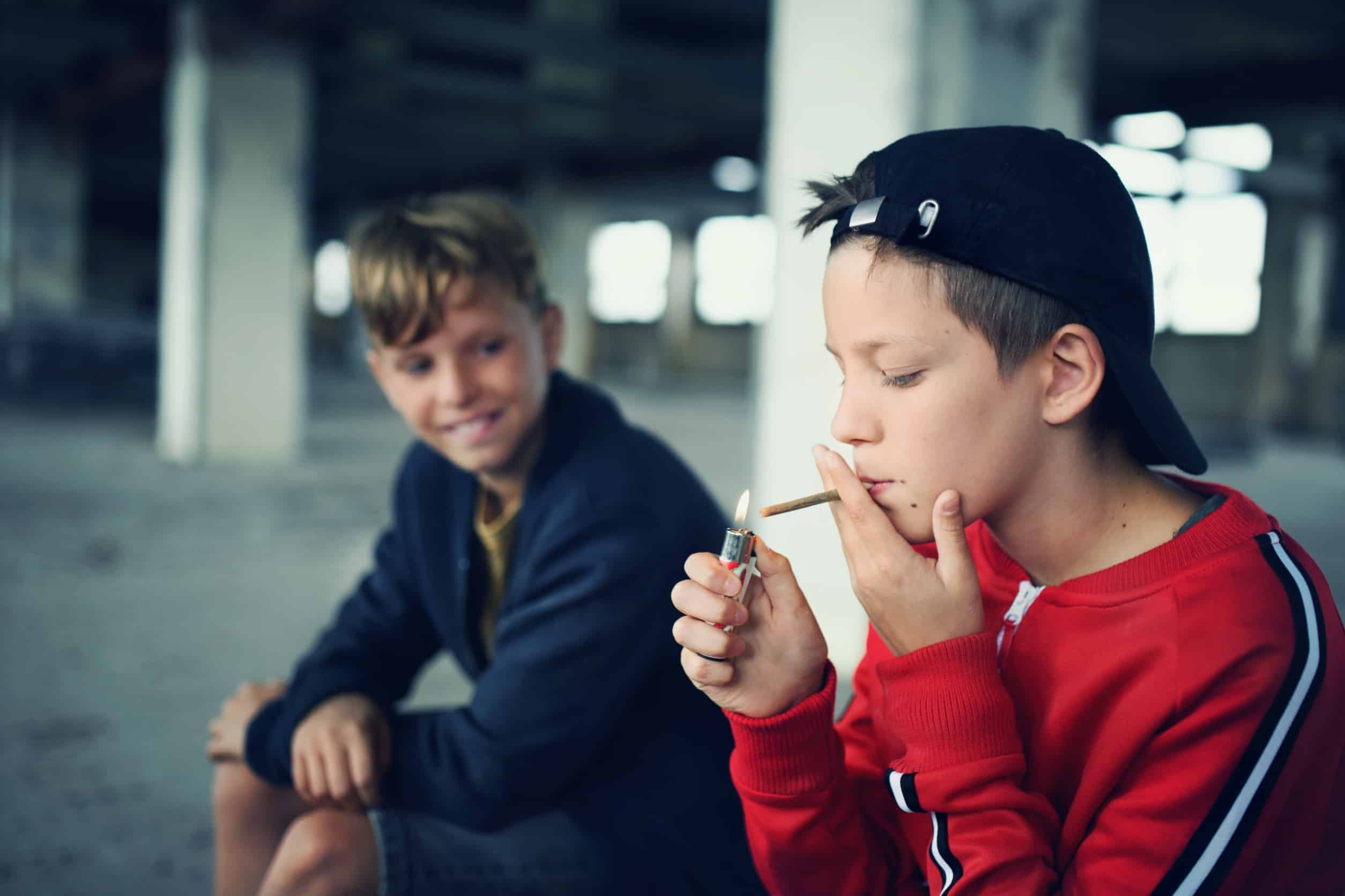 Two young adolescent boys smoking marijuana in a parking garage
